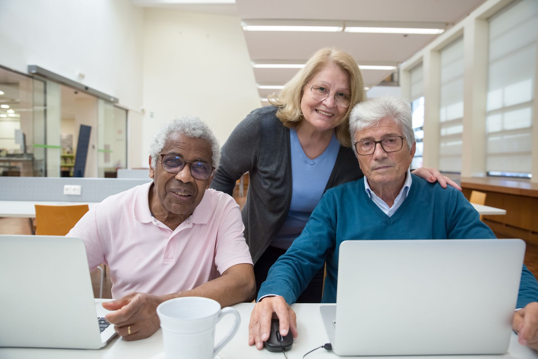 trois seniors souriants devant des ordinateurs portables lors d'un atelier informatique en médiathèque
