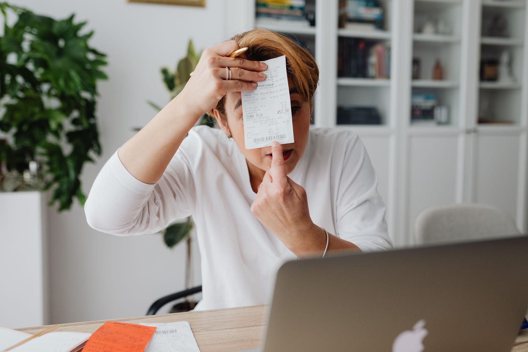 dirigeante de PME assise à son bureau, consultant un reçu de facturation près d'un ordinateur portable