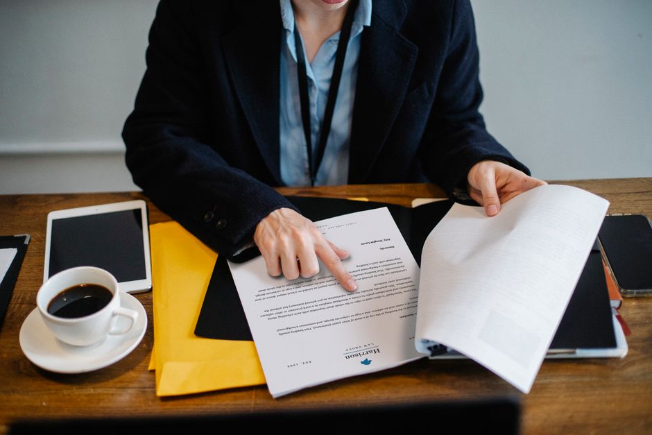 High angle of crop faceless woman in formal wear sitting at wooden table with tablet and coffee and reading documents