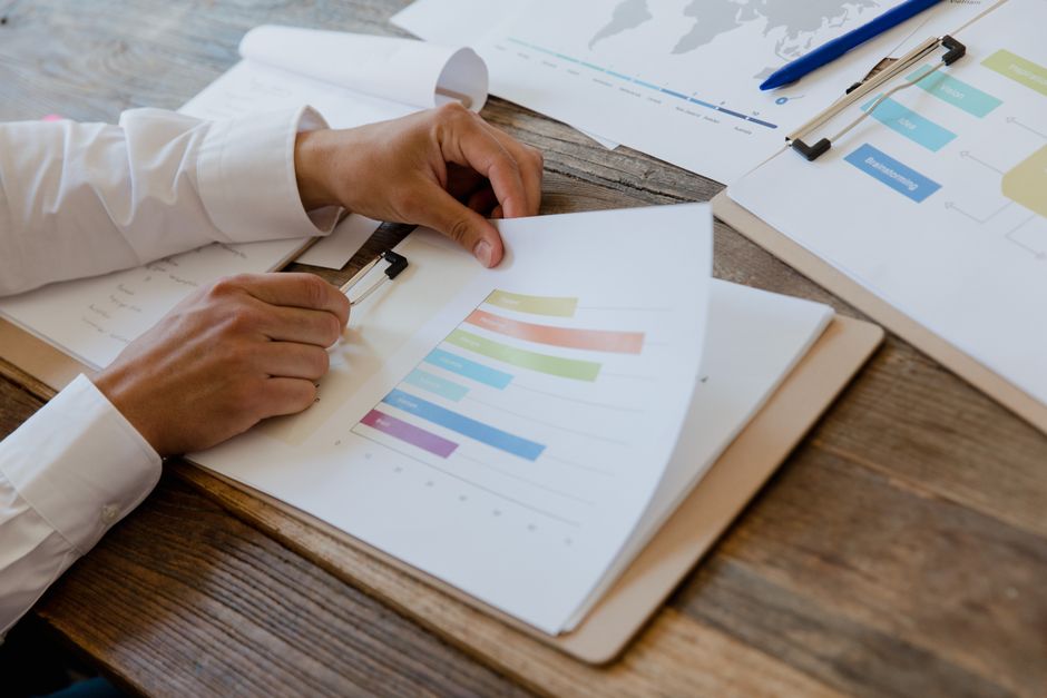 Close-up of hands reviewing business report with colorful charts and graphs on a wooden desk.
