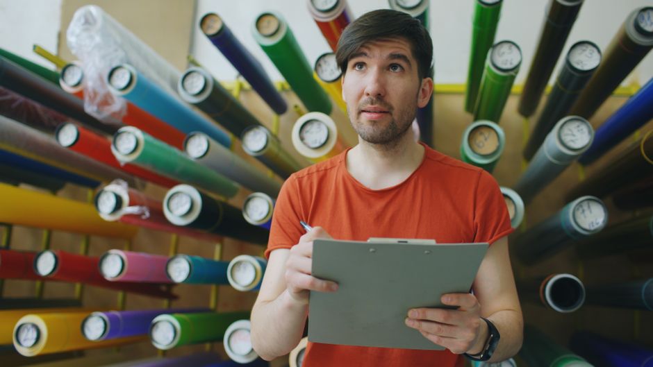 Young man in a vibrant workshop examining materials with a clipboard.