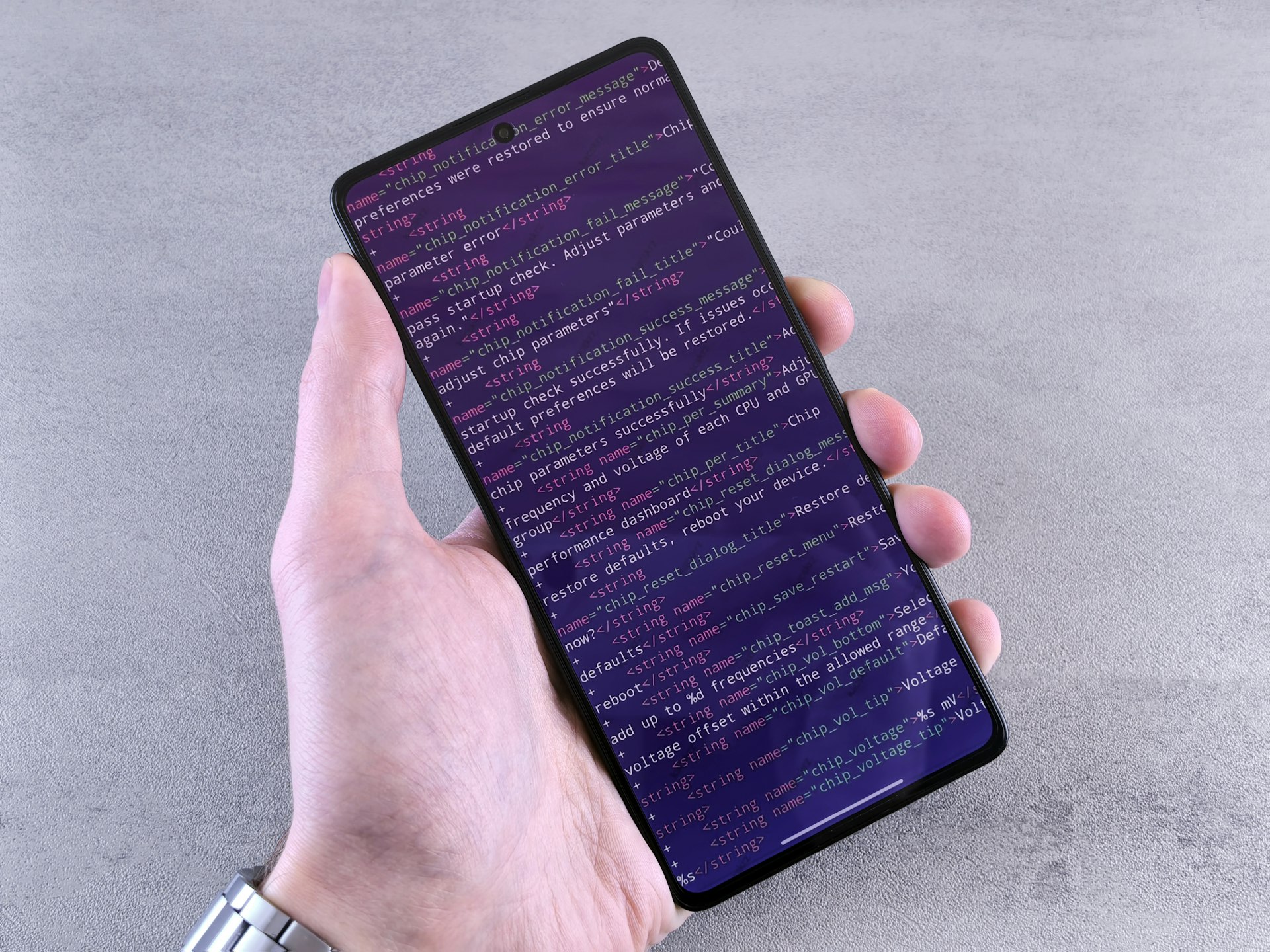 main tenant un smartphone dont l'écran affiche des lignes de code